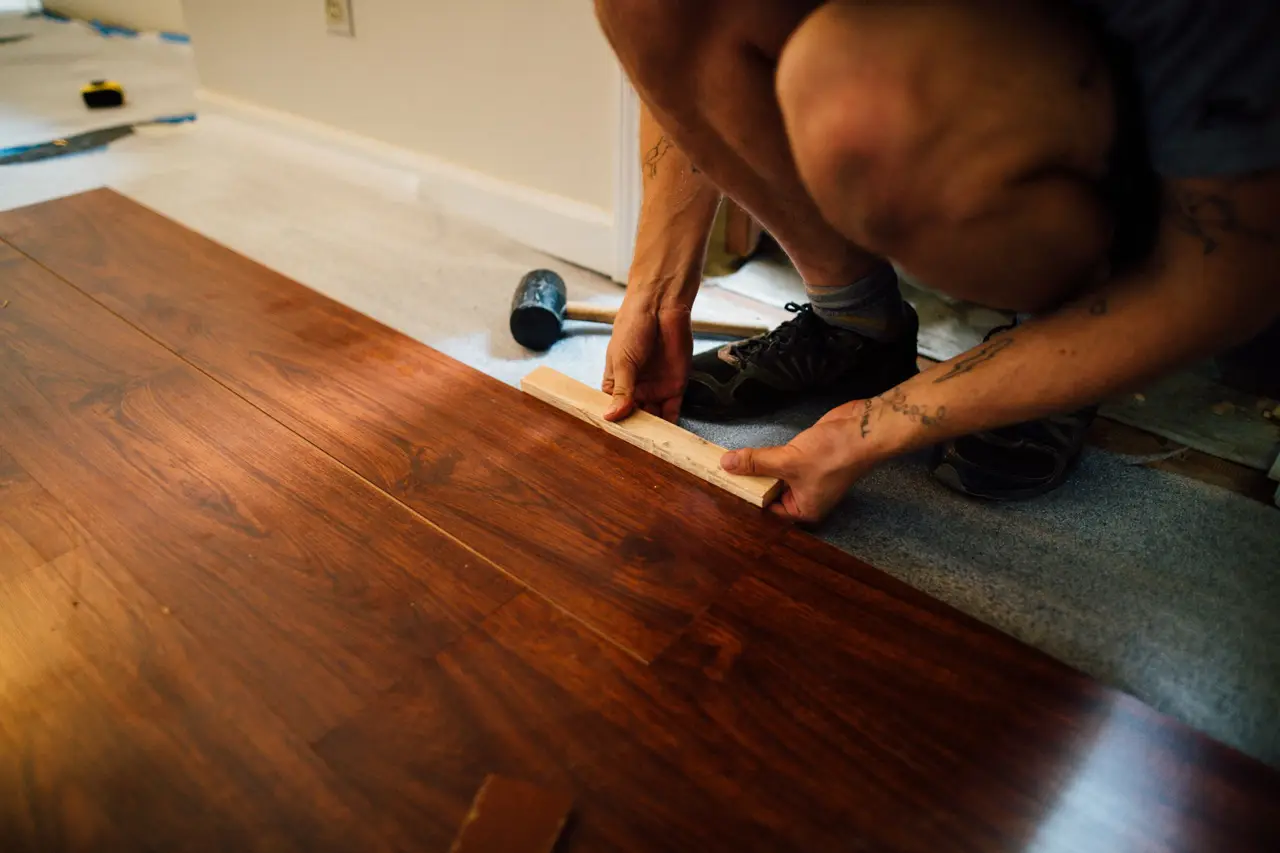 Um instalador de pisos encaixando uma régua de piso vinílico no lugar numa sala iluminada