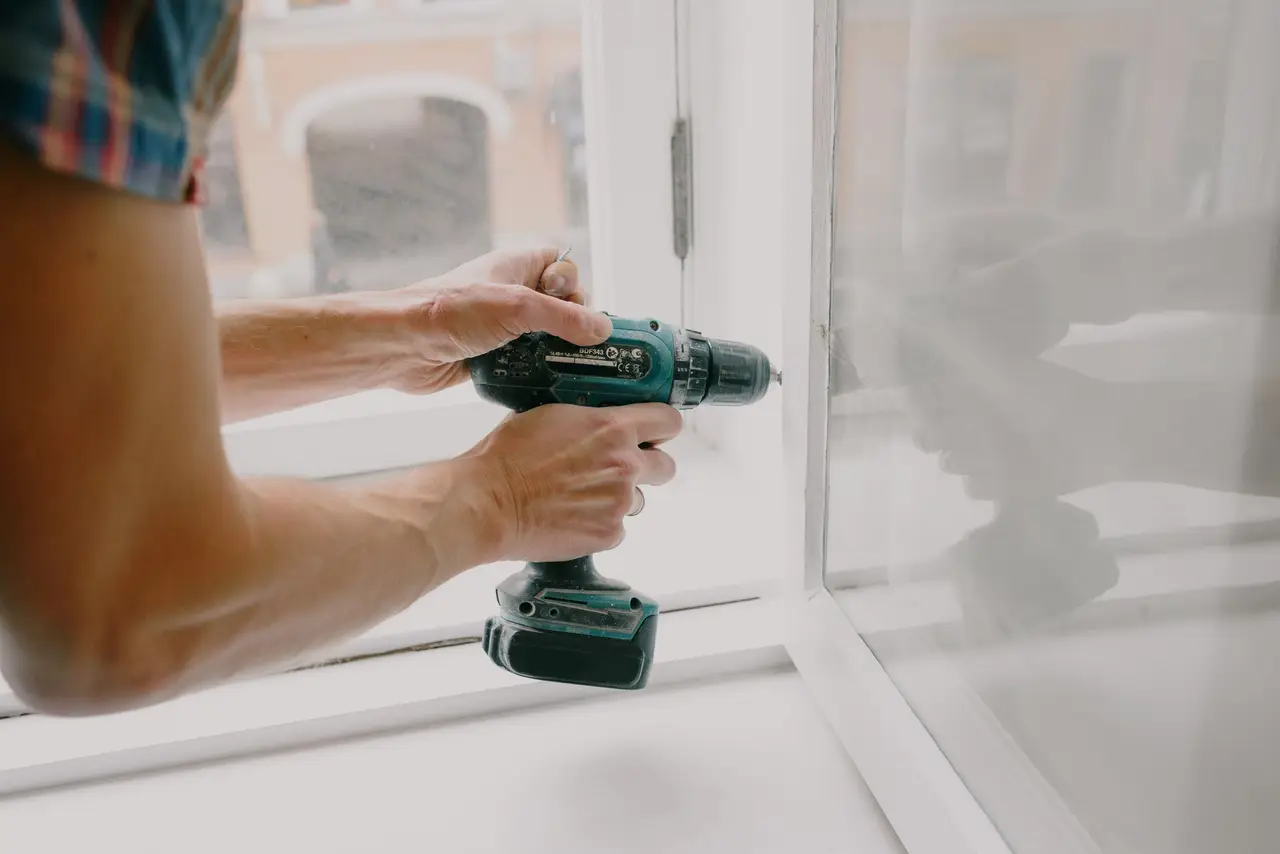A handyman in a tool belt fixing a cabinet hinge inside a home