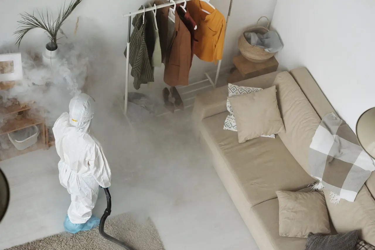 A pest control technician in uniform spraying along the baseboard of a home's exterior foundation