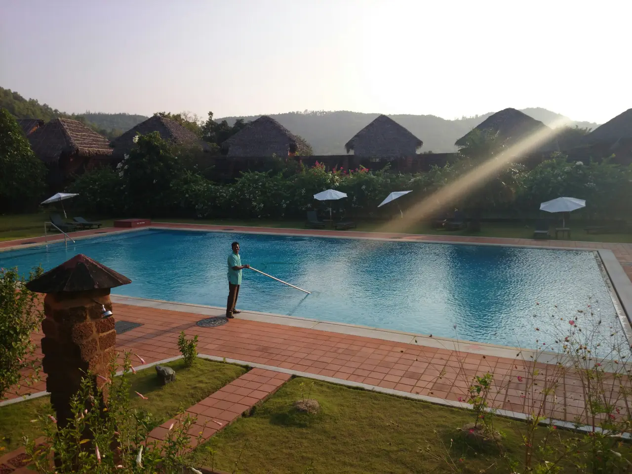 Um técnico de piscinas recolhendo folhas e medindo a água de uma piscina de quintal em um dia ensolarado
