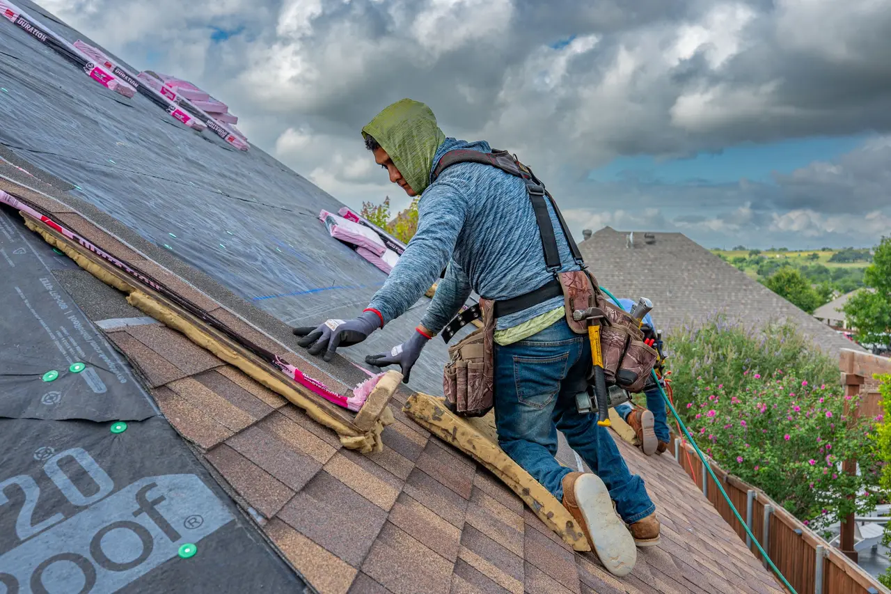 A roofing crew laying shingles on a steep residential roof on a clear day
